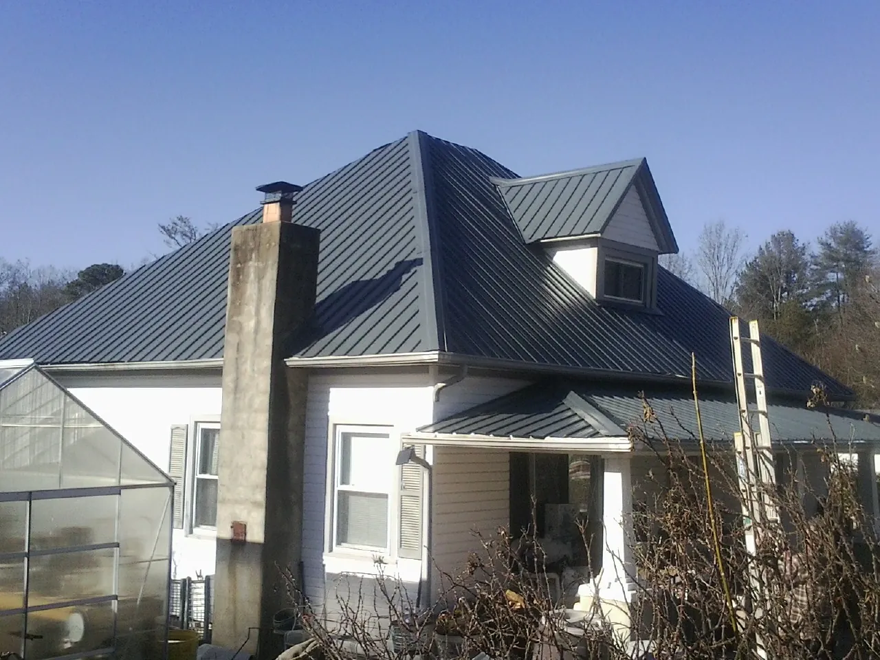 Dark blue standing seam metal roof on a white farmhouse with dormer — Slate & Tile Roof Repair by Roofing Brothers in Riverview