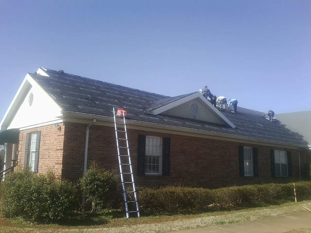 Crew tearing shingles off a brick ranch roof with a ladder set — Emergency Roof Repair work by our crew in Riverview
