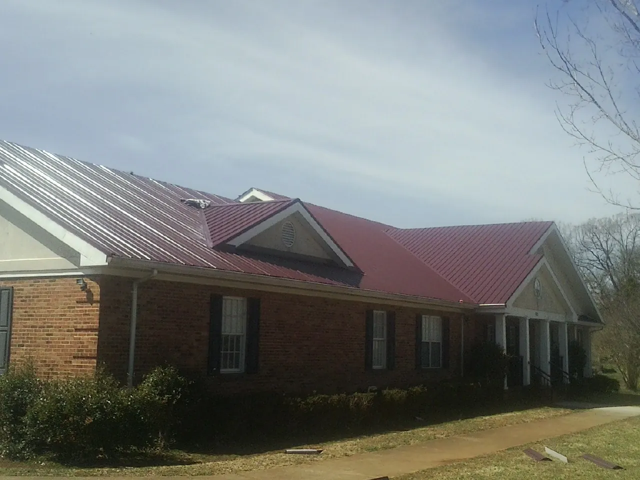 Red metal roof with gabled entries on a long brick building, from a Hail Damage Roof Repair job in Riverview