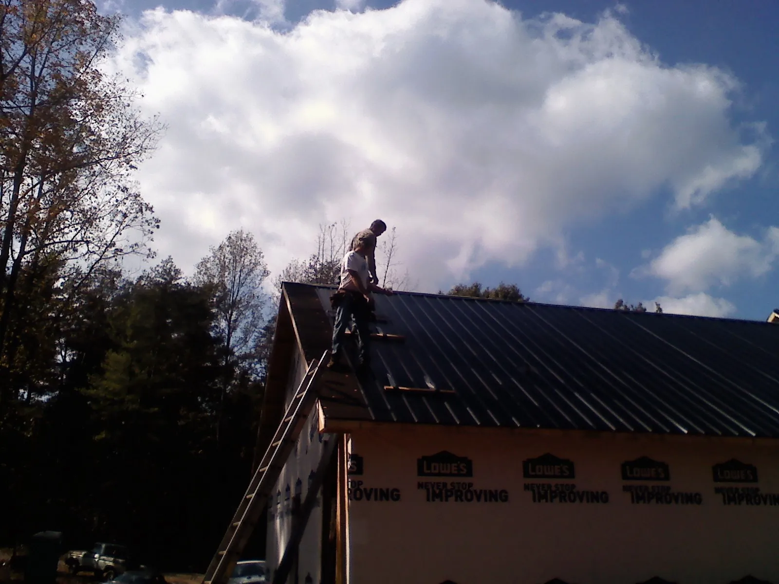 Roofer fastening dark metal panels high against a cloudy sky, from a Roof Inspection job in Riverview